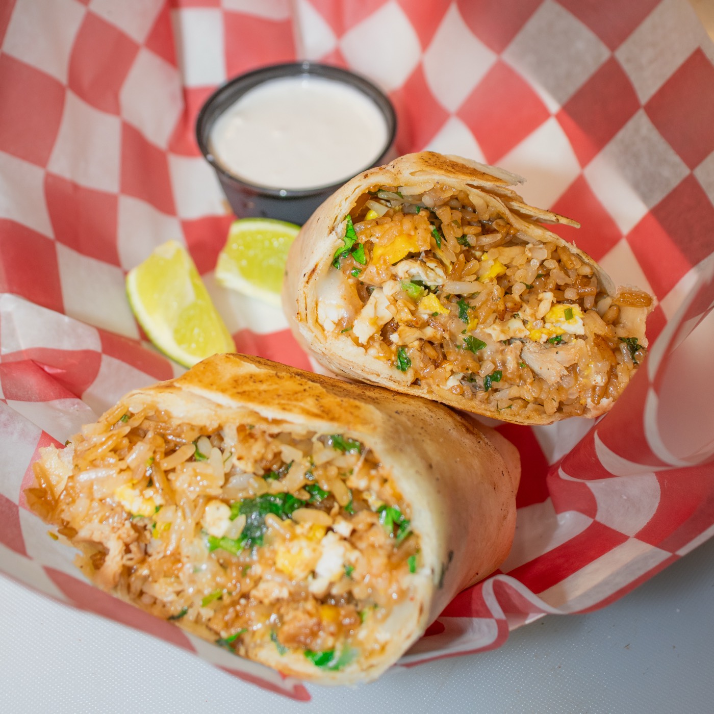 Bibimbap burrito cut open in a red basket with lime and dipping sauce